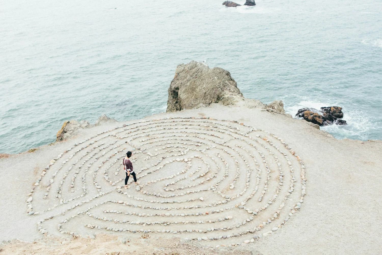 Personne marchant dans un labyrinthe de pierres face à la mer