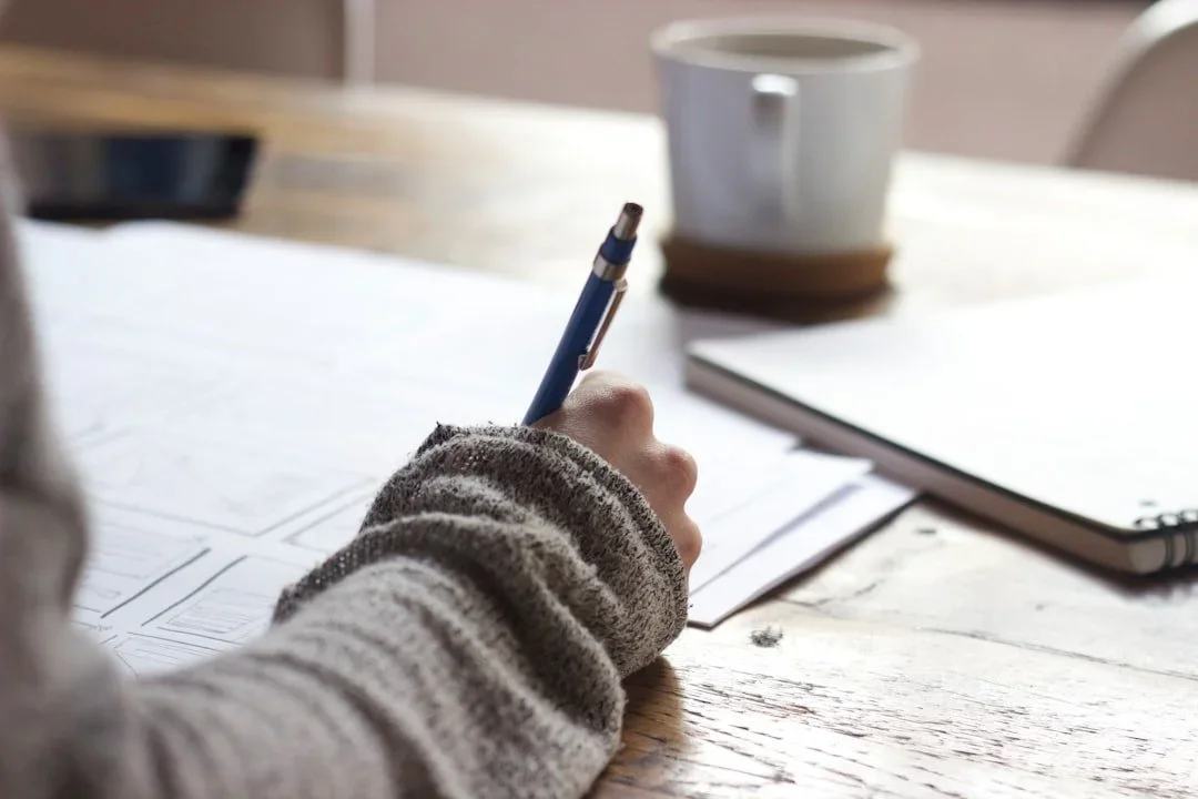 Main qui écrit un manifeste au stylo sur une feuille, tasse de café posée sur le bureau